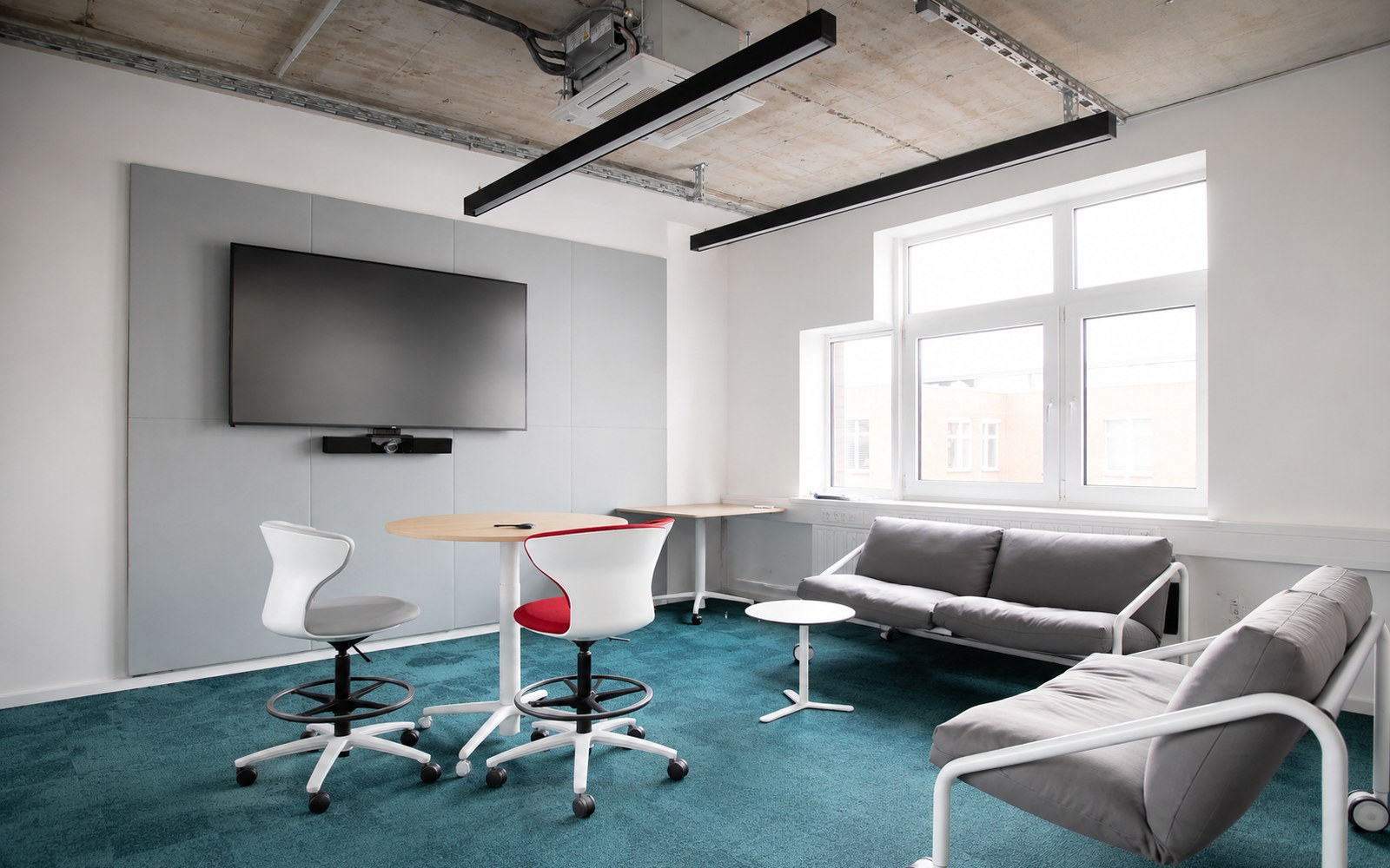 Lounge- und Meetingbereich mit türkisfarbenem Teppich, Akustikelementen und flexiblen Sitzmöglichkeiten