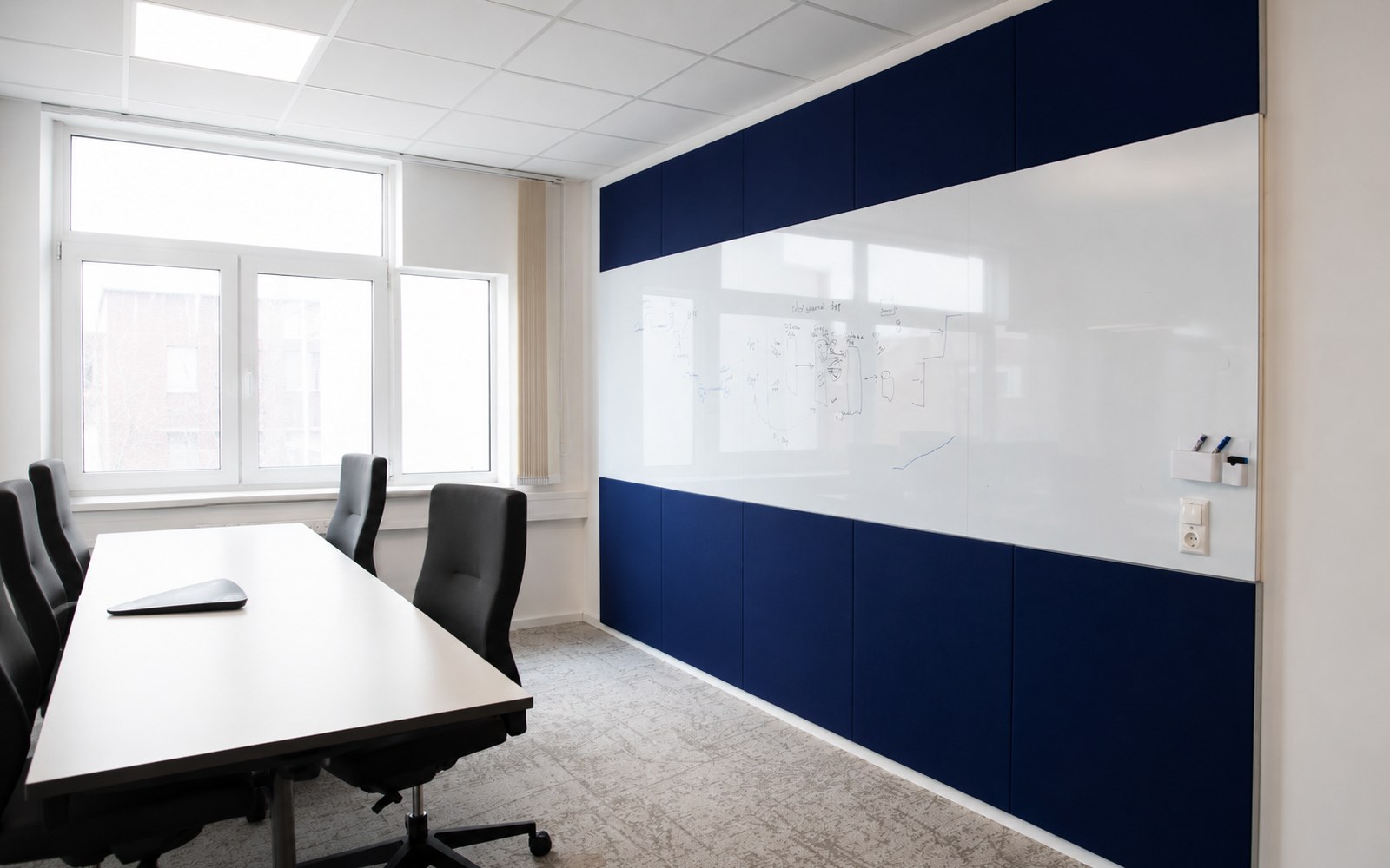 Besprechungsraum mit großflächiger Whiteboard-Wand und blauen Akustikelementen