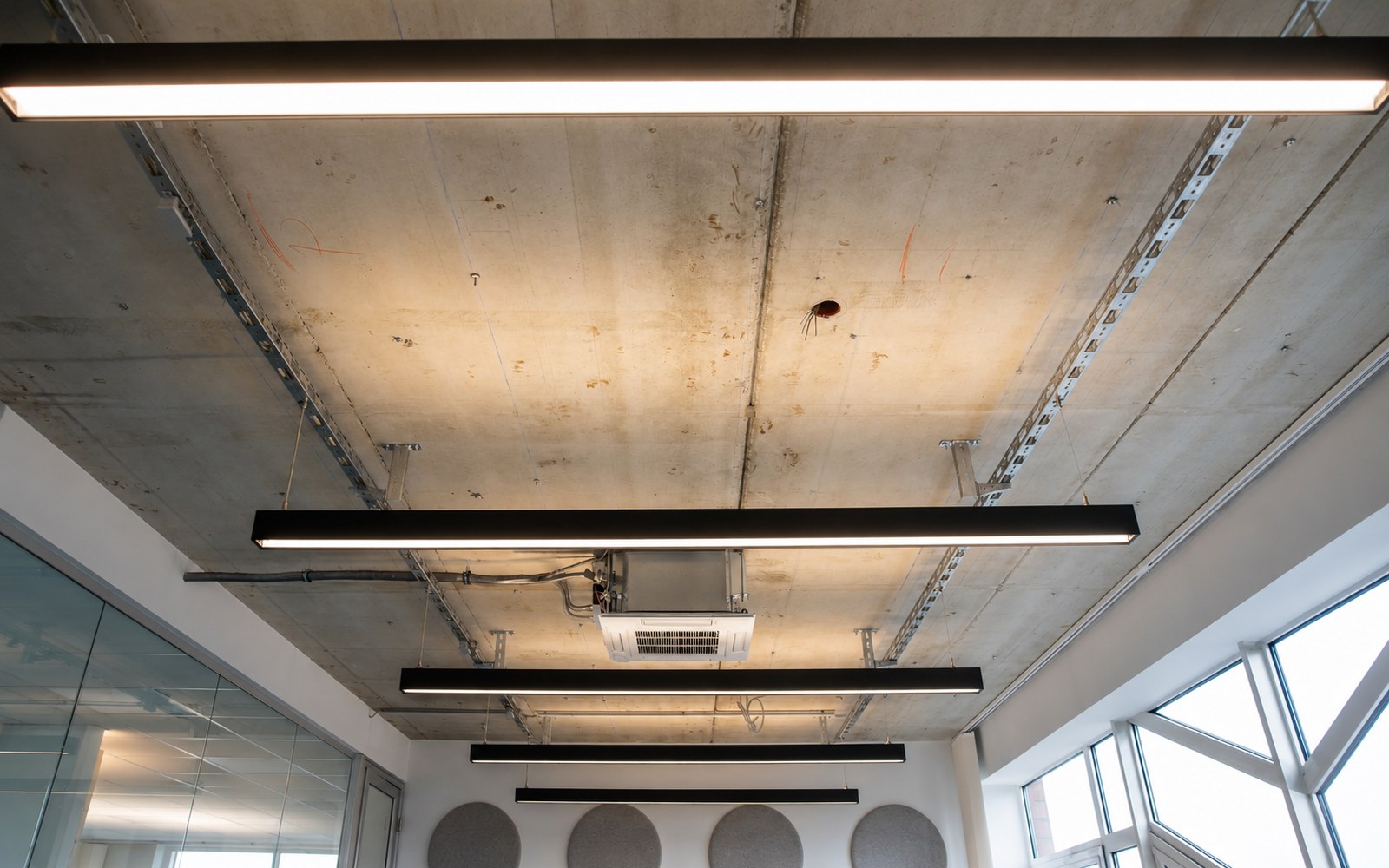 Rohdecke mit linearen Leuchten und sichtbarer technischer Infrastruktur